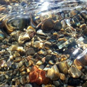 Macro photo of swirling water distorting the gentle pebbles below the surface.
