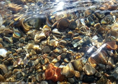Macro photo of swirling water distorting the gentle pebbles below the surface.